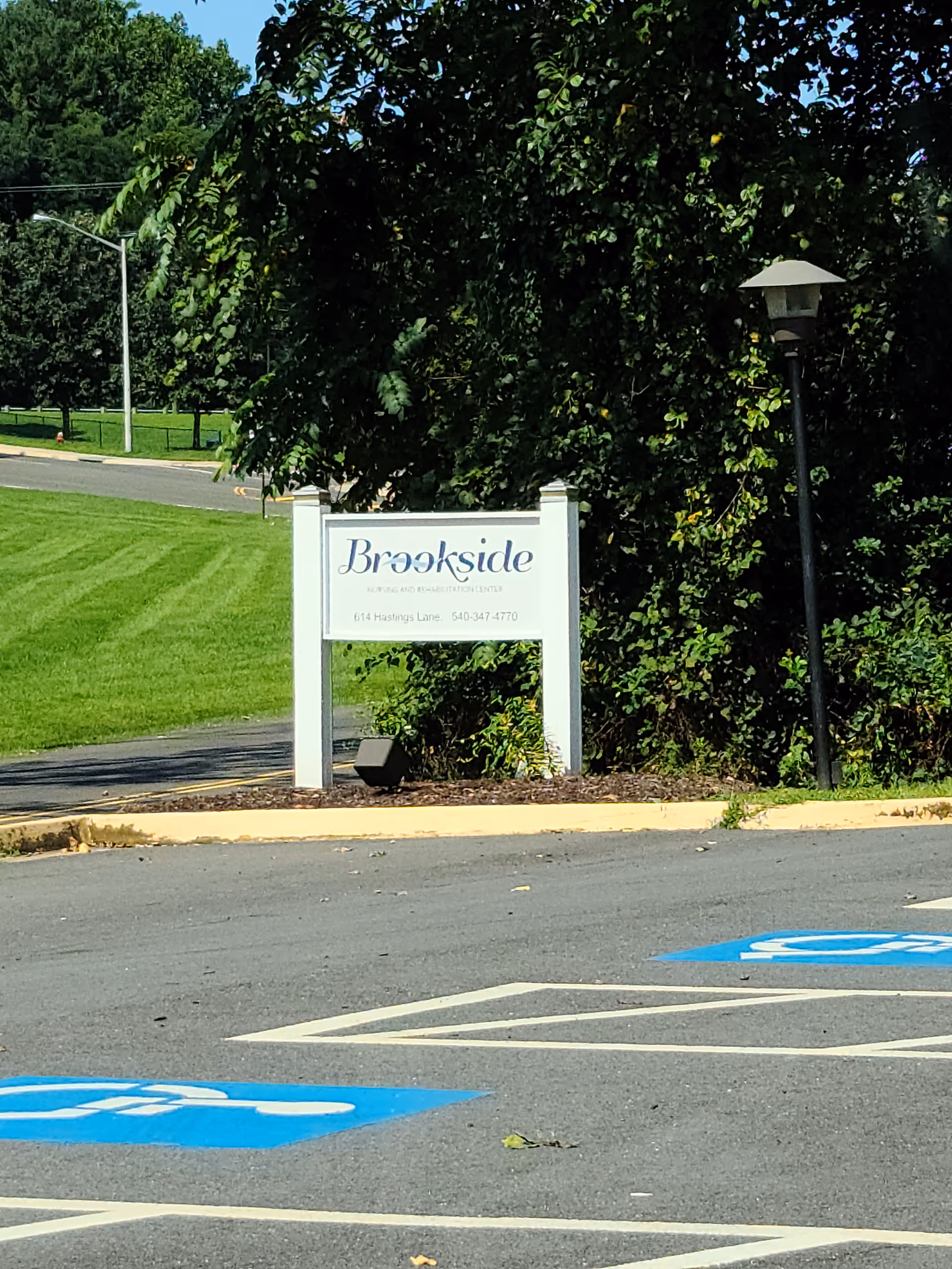 Exterior view of Brookside Rehab & Nursing Center sign amid greenery and a parking lot.