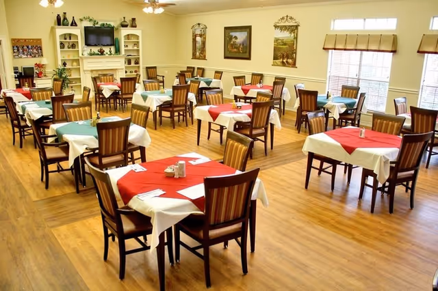 Bright communal dining room with multiple round tables set with red and green tablecloths and wooden chairs.