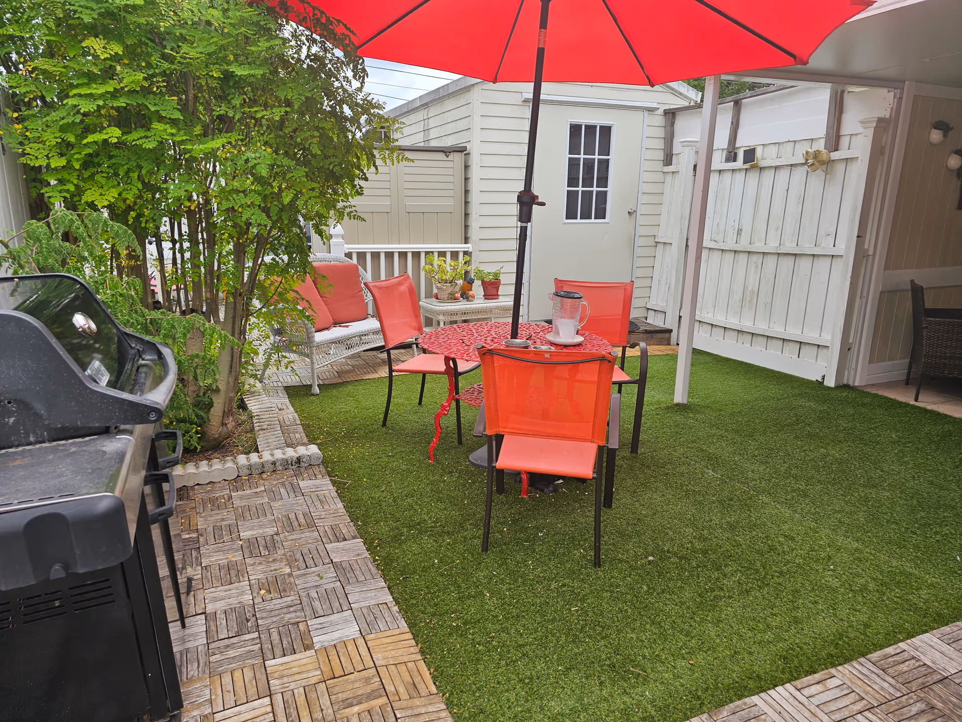 Outdoor patio with red chairs, umbrella, grill, and artificial turf.