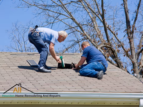Two workers on a sloped roof installing a vent, company logo visible.