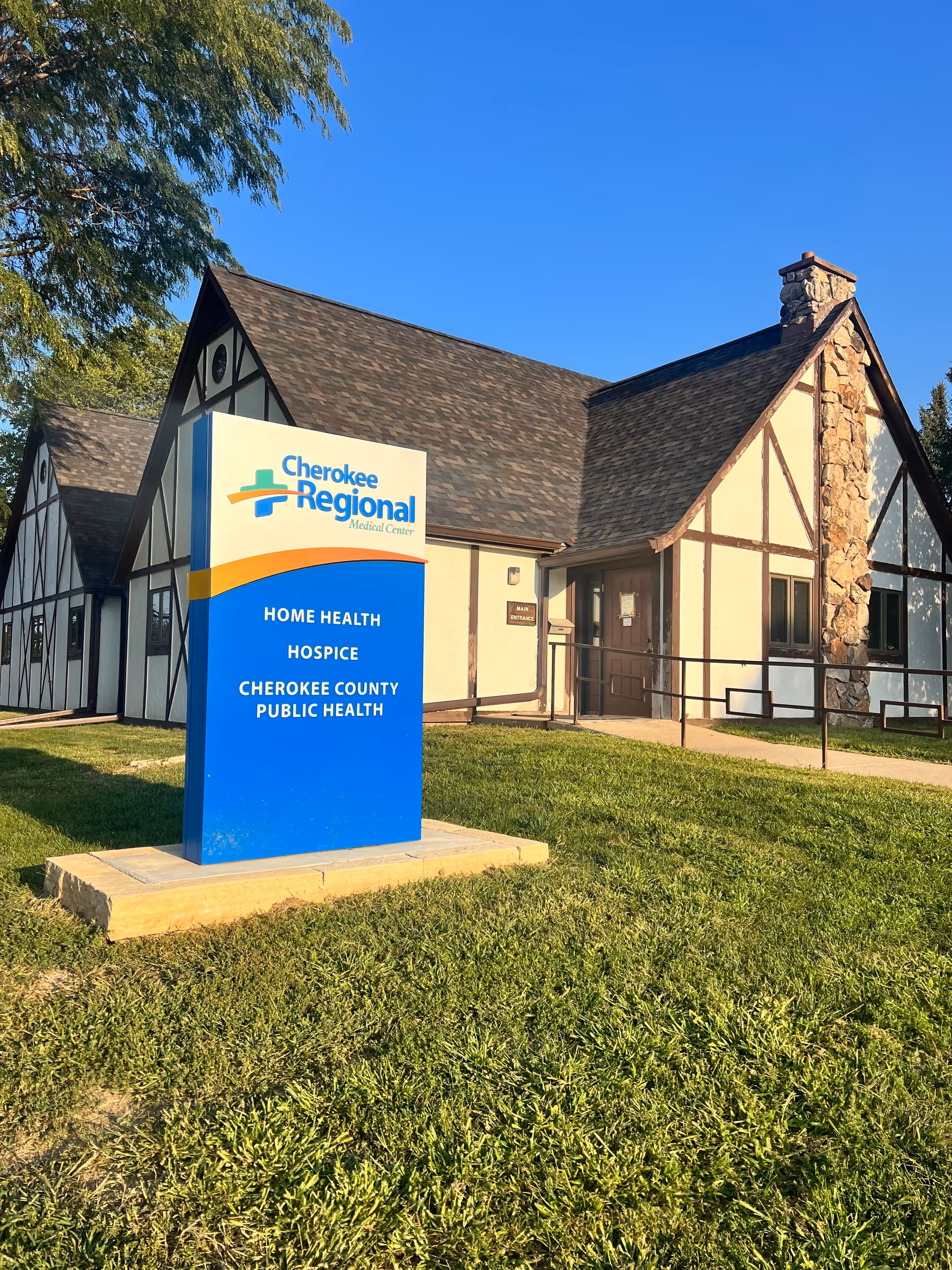 A Tudor-style medical facility with a blue Cherokee Regional sign on a grassy lawn