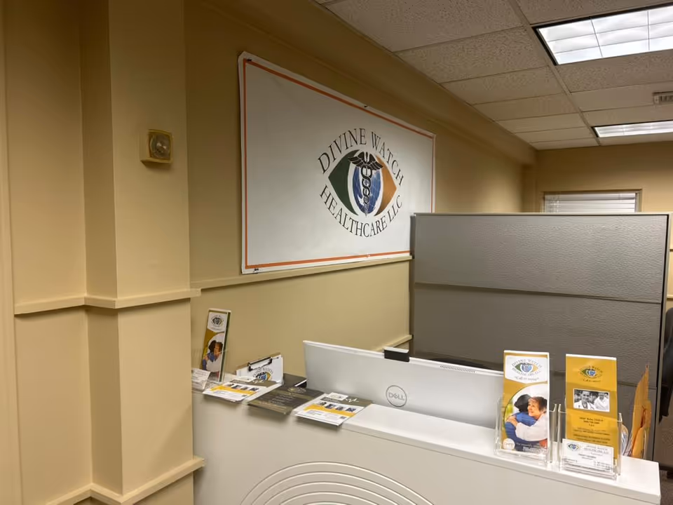Reception area with a white desk, gray divider panels, and a Divine Watch Healthcare sign.