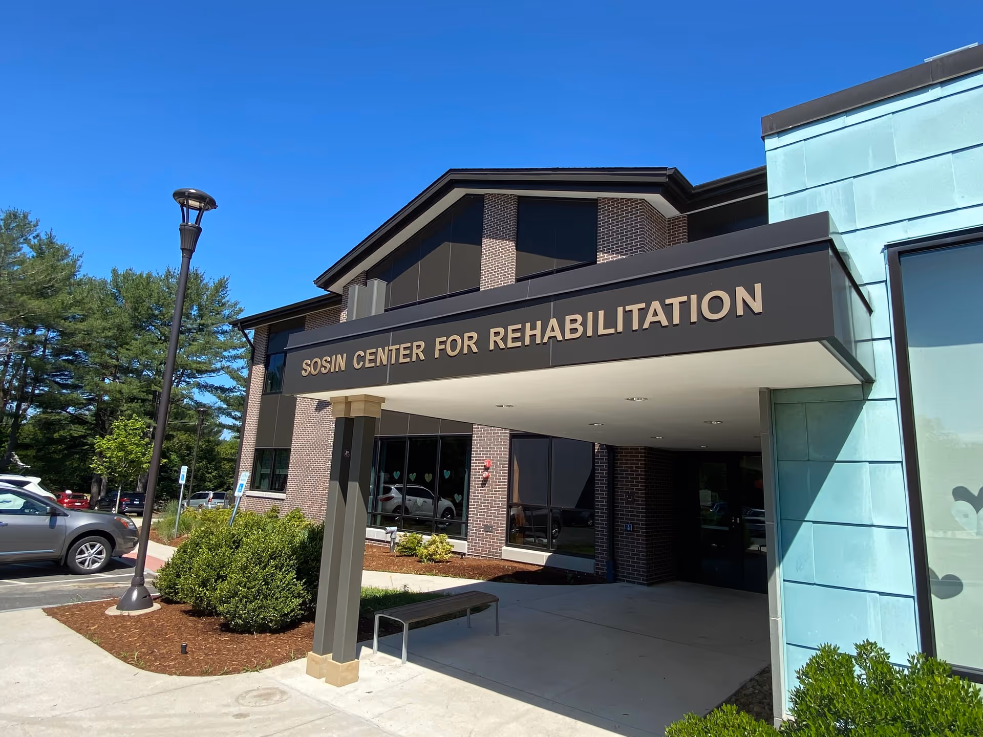 Exterior entrance of Sosin Center for Rehabilitation with canopy sign, brick facade, and parked cars.