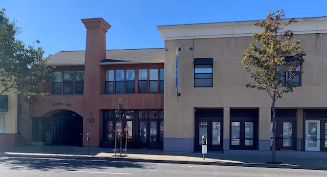Exterior view of Elders Inn building with a beige and brown facade, multiple windows, two small trees in front, and a clear blue sky above.