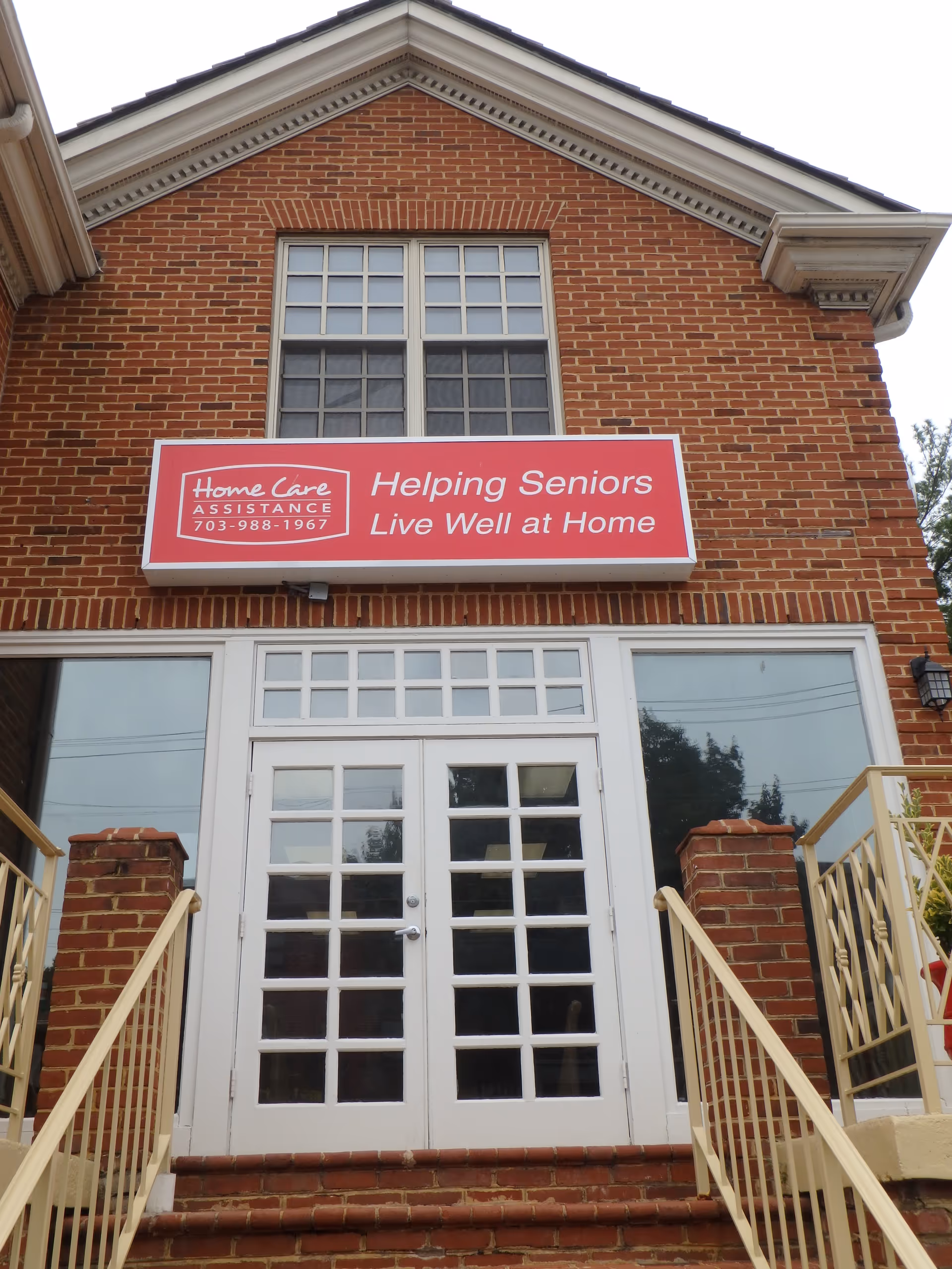 Red brick senior care building with double white doors and a large sign.