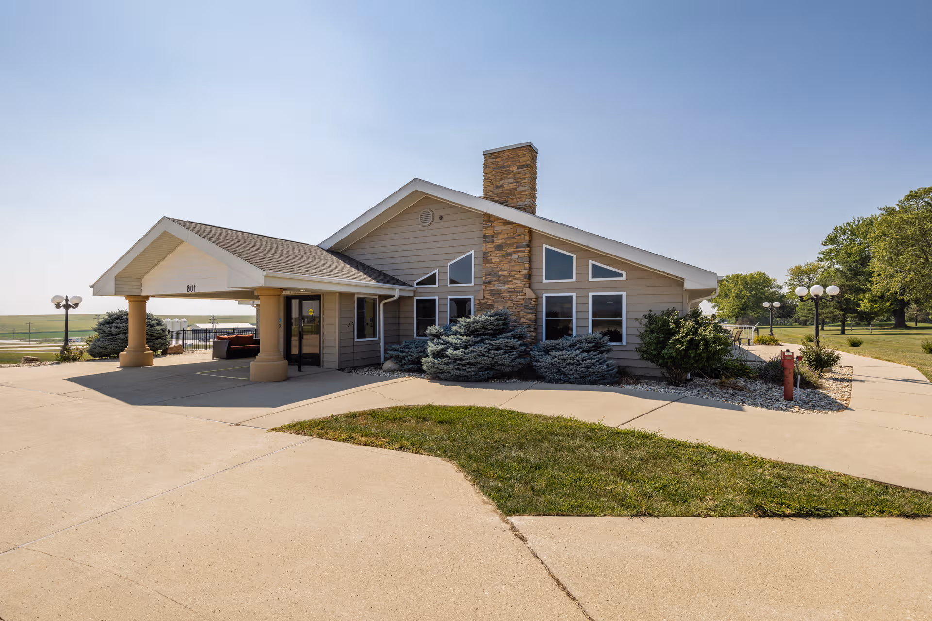 Single-story senior living facility with a stone chimney, covered entrance, and surrounding landscaping.