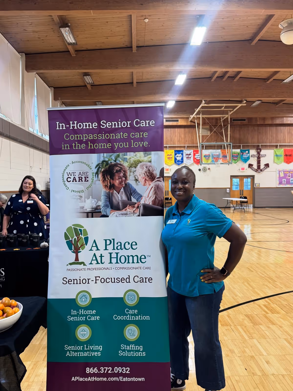 A Place At Home Eatontown banner indoors with a smiling staff member beside it