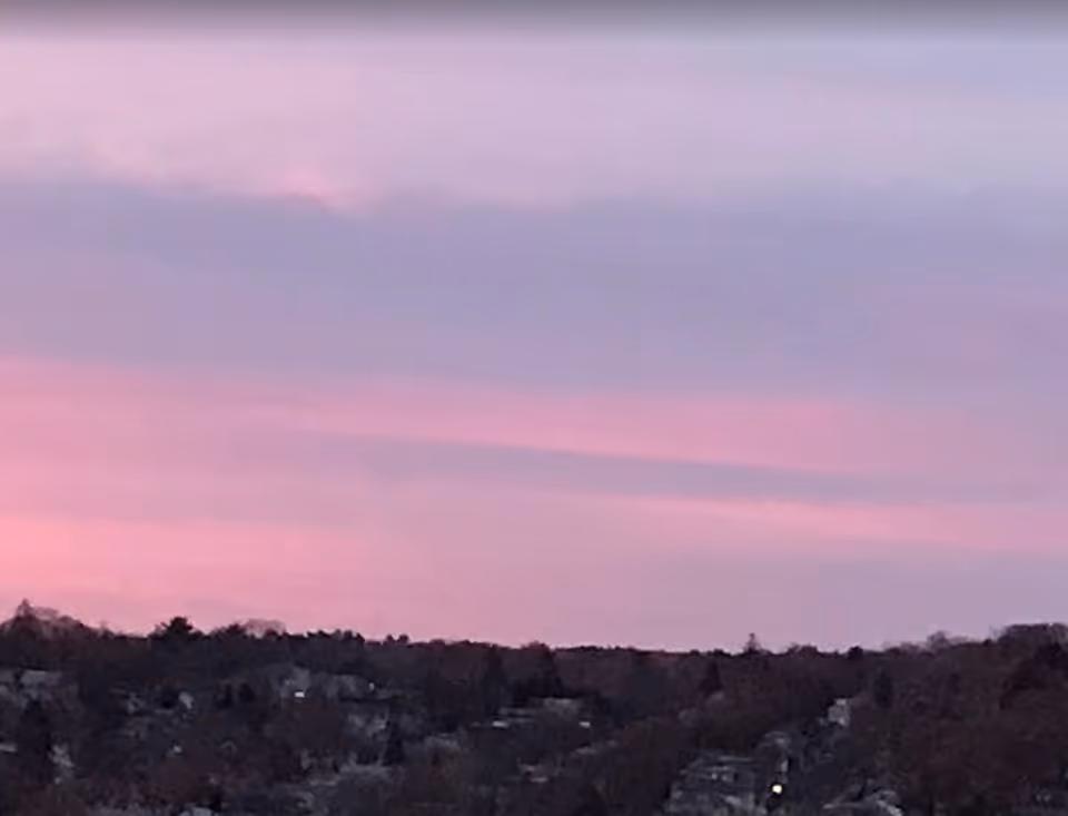 A scenic view of a residential area with houses and trees under a pink and purple sunset sky.
