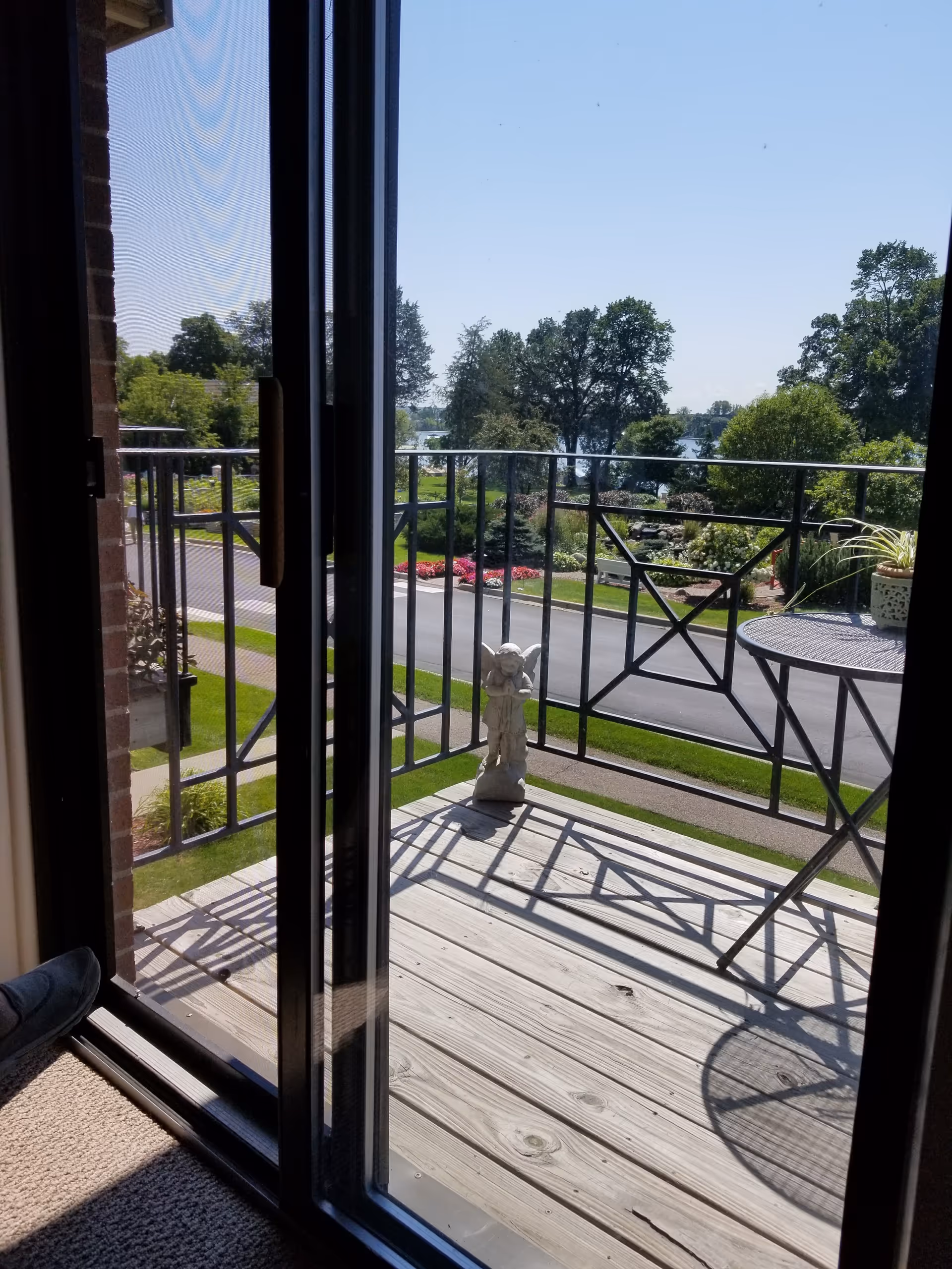 View from a sliding glass door onto a wooden balcony with a table, railing, and statue.
