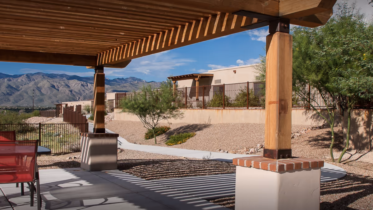 Outdoor patio under a wooden pergola with red chairs and desert landscaping