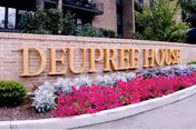 Brick wall with Deupree House sign and colorful flower bed.