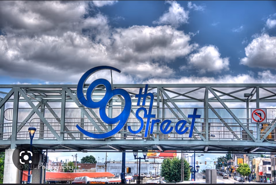 Blue 69th Street sign mounted on a metal pedestrian bridge over a city street