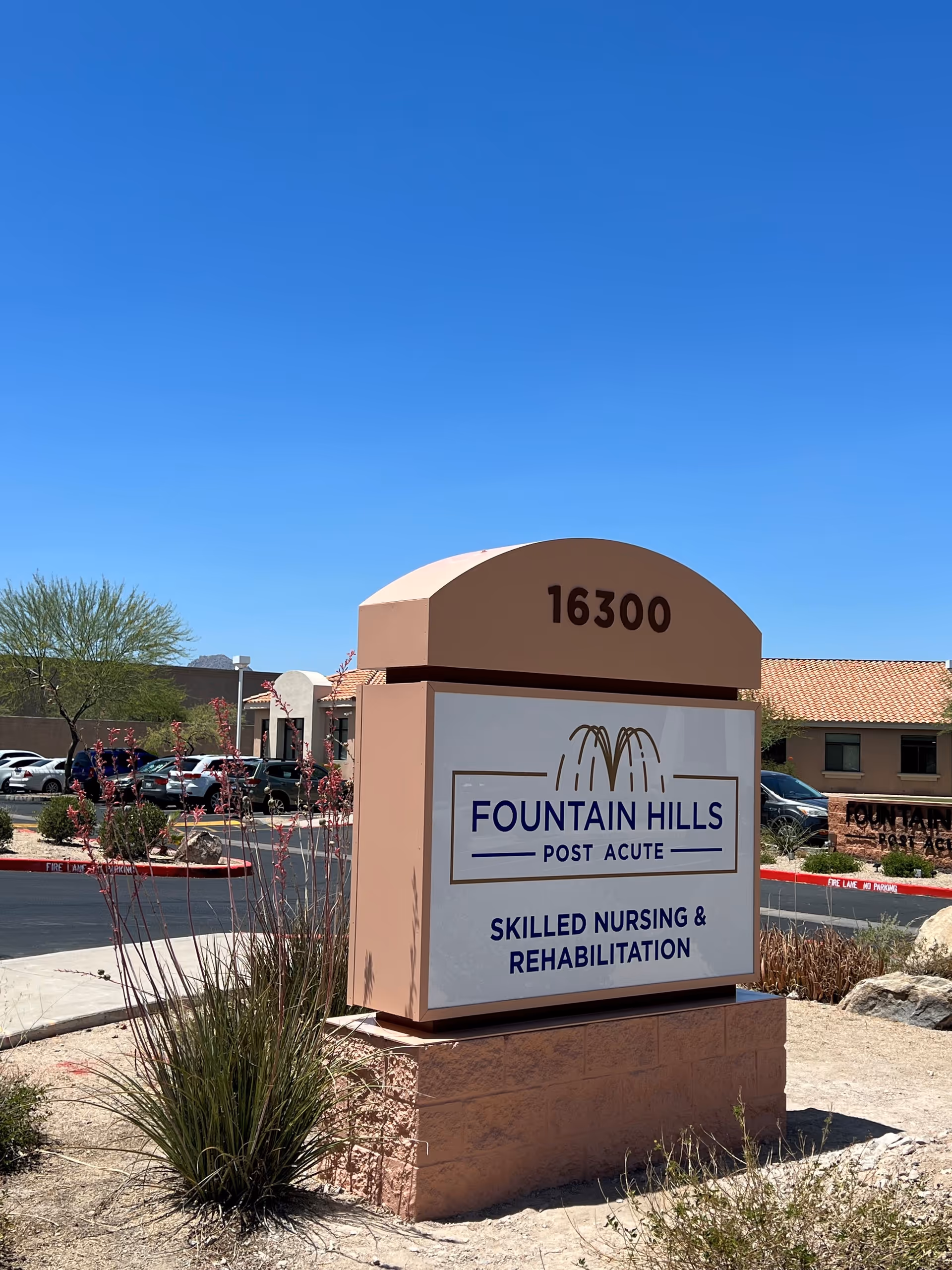 Exterior view of Fountain Hills Post Acute sign with building, desert landscaping, and cars.