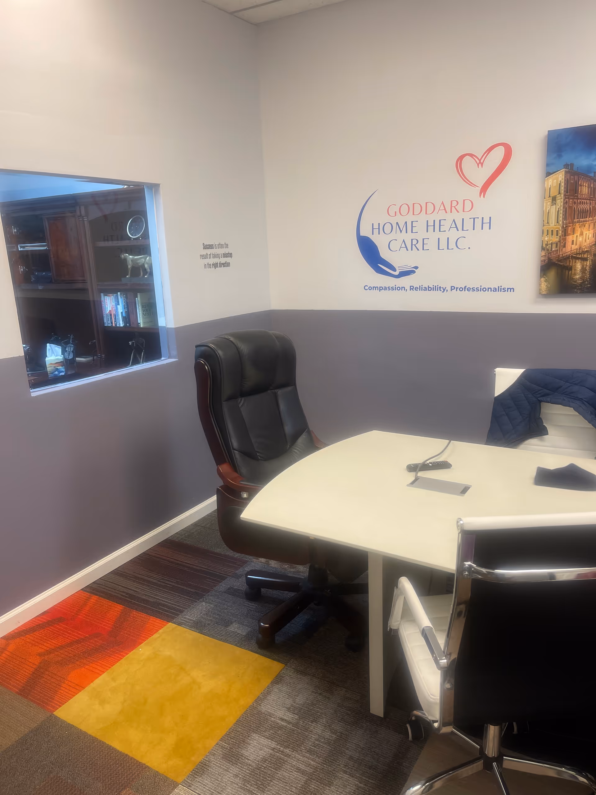 Office space with desk, black executive chair, and Goddard Home Health Care LLC logo on wall.