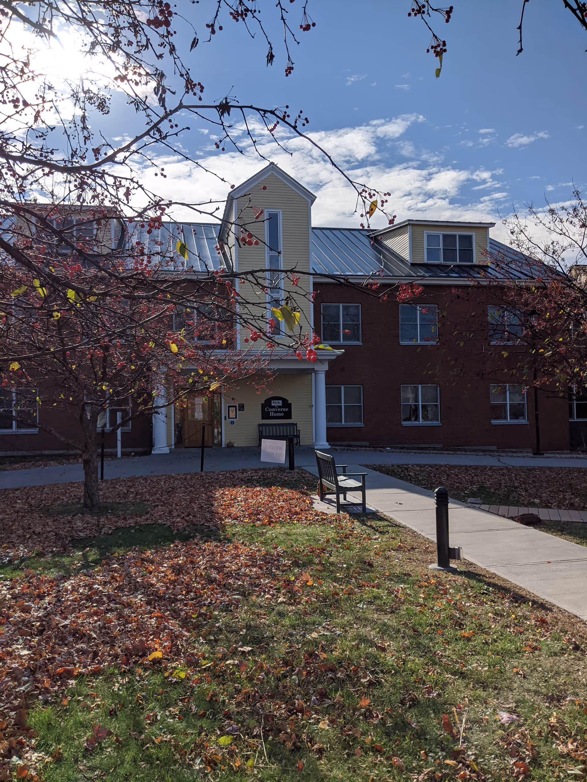 Front view of Converse Home senior living building with walkway, bench, and autumn leaves.