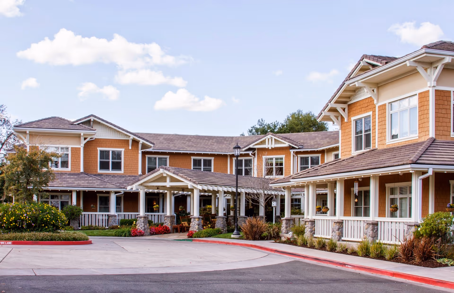 Exterior front of a two-story senior living facility with a covered entrance, wraparound porch, and landscaped driveway.
