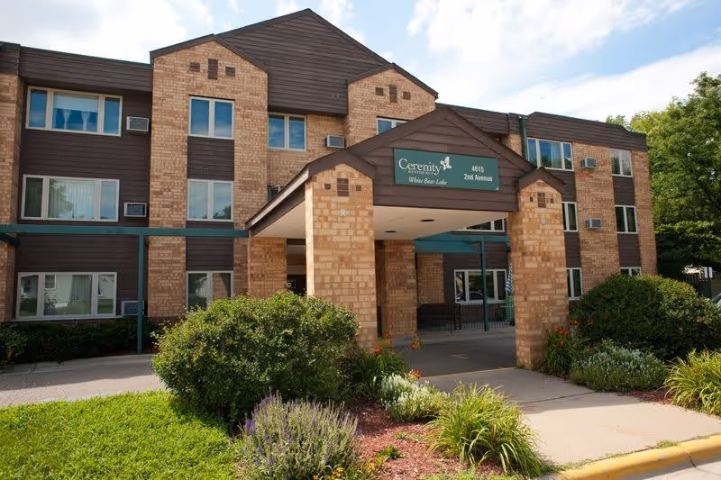 Exterior front view of Cerenity Residence White Bear Lake, a three-story brick building with a covered entrance and landscaped greenery in front.