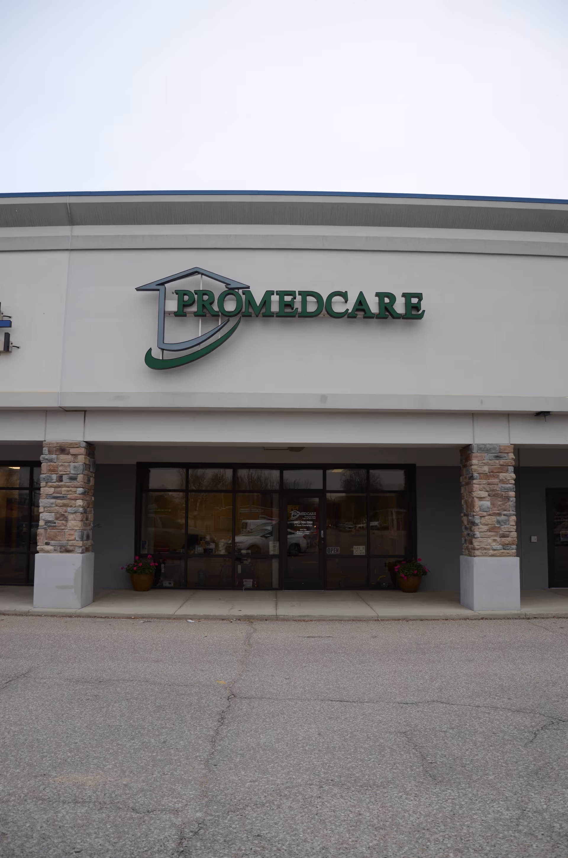 Promedcare building entrance with logo, stone columns, glass doors, and potted plants.