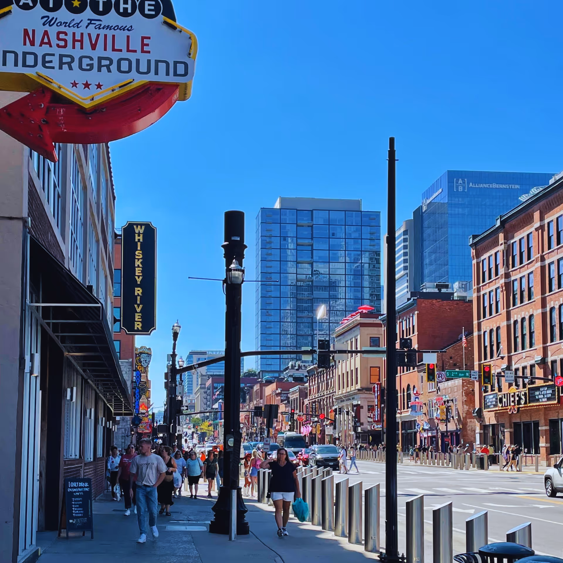Busy urban street in Nashville with pedestrians, signs, and tall modern buildings.