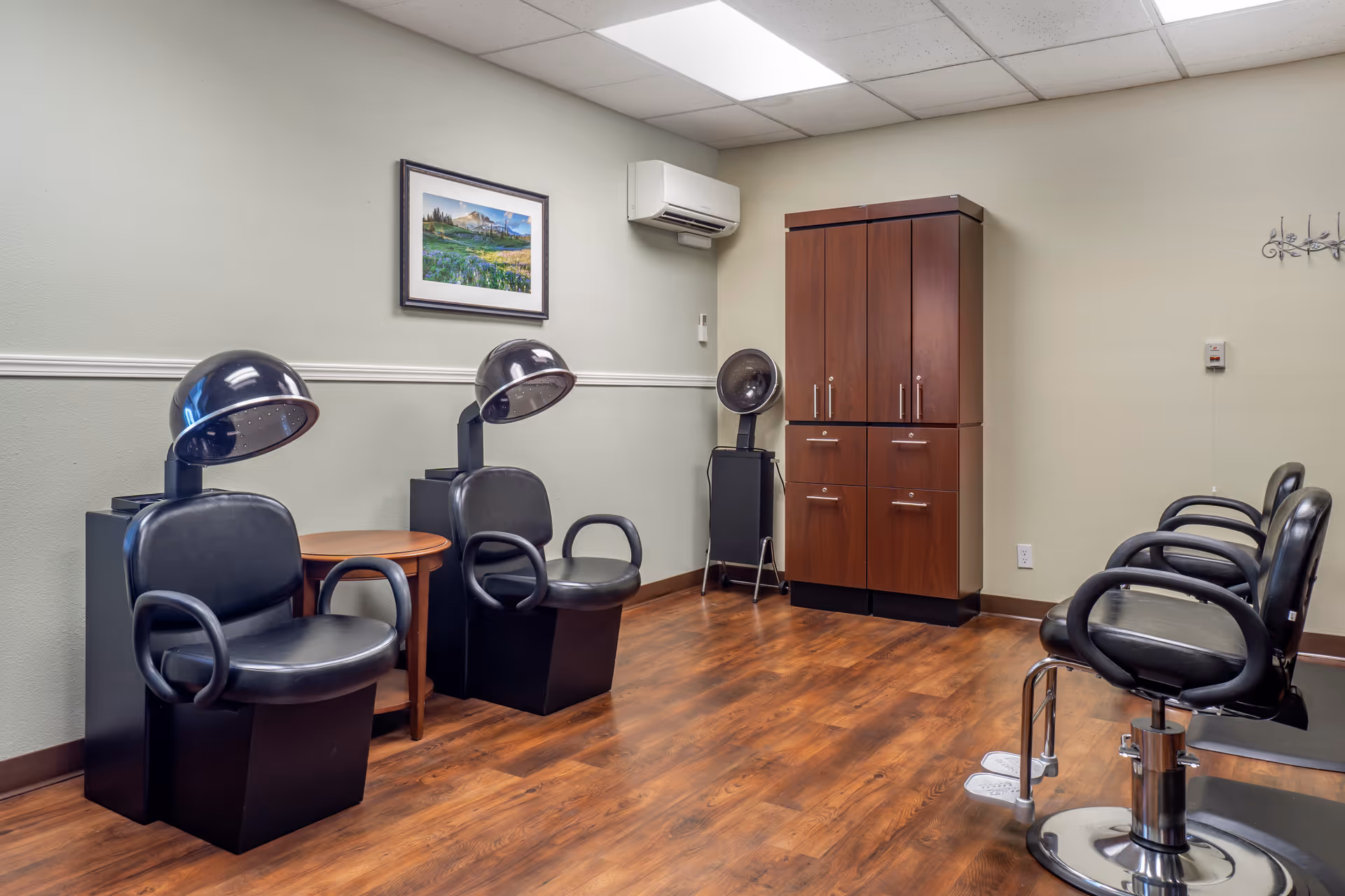 Salon area with black hair dryers, chairs, wooden cabinets, and laminate flooring.