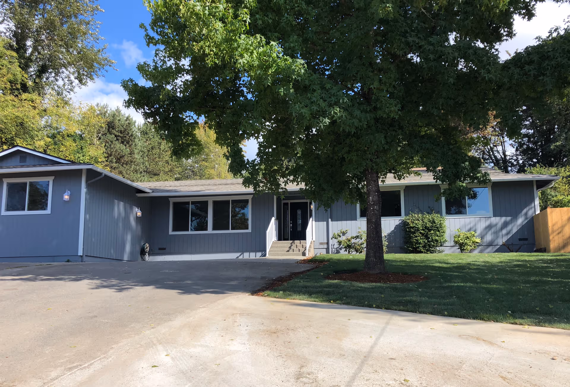 Single-story blue senior care facility front view with driveway and large tree