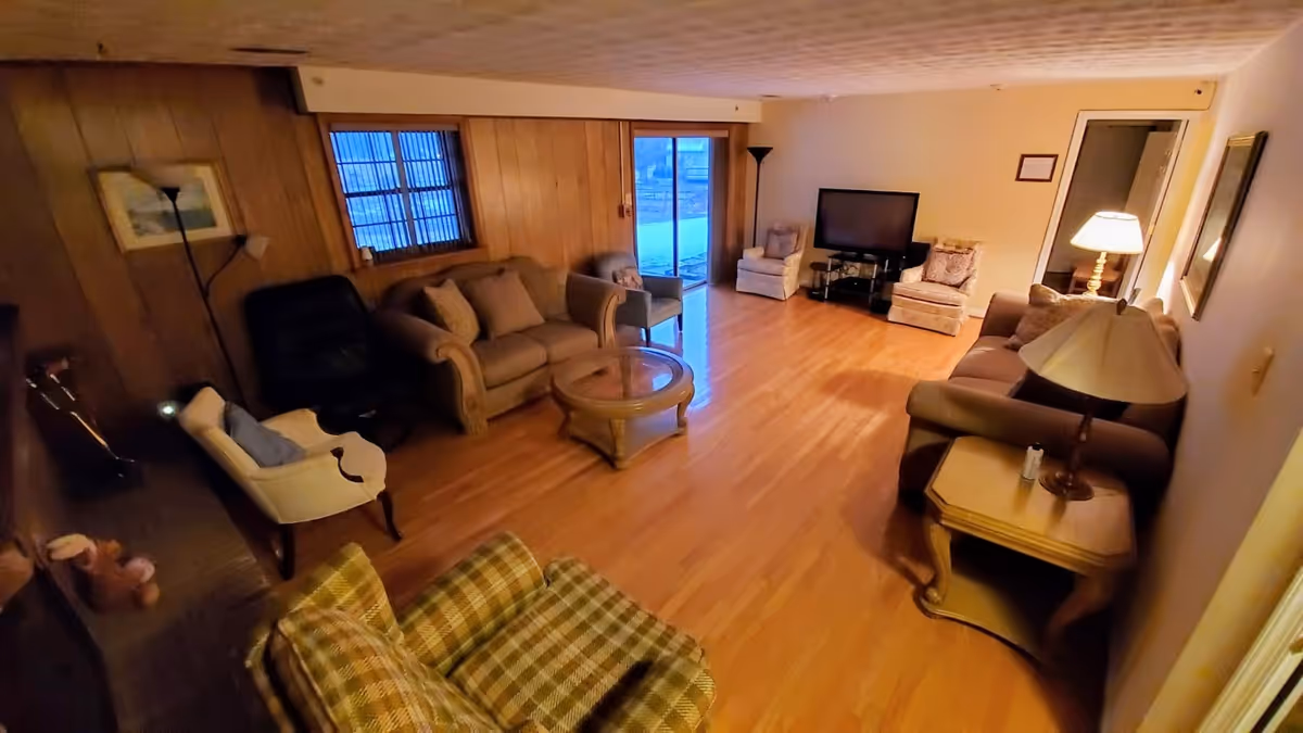 Cozy living room in Homecrest Assisted Living with wood paneling, sofas, chairs, and a TV.