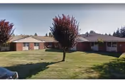 Single-story brick senior living building with a well-kept lawn and burgundy trees.