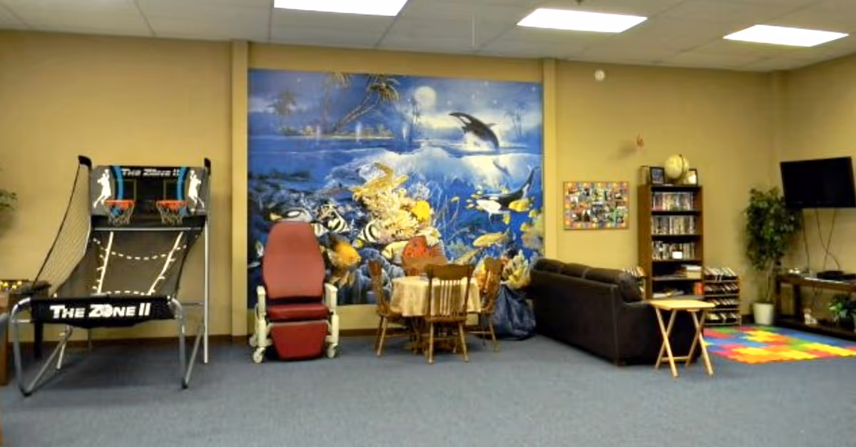 Indoor activity lounge with ocean mural, arcade basketball game, seating, sofa, bookshelf, TV, and rug.