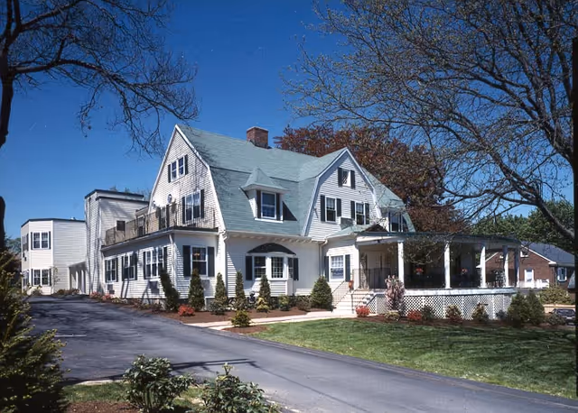 A large white nursing home with a peaked roof, front porch, and landscaped grounds.