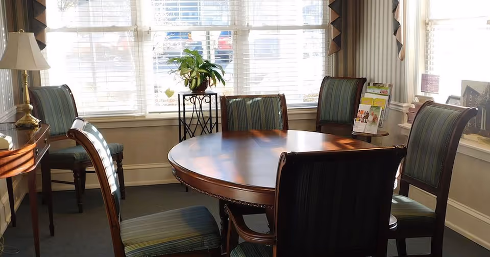 Bright dining room with round wooden table and striped chairs by windows.