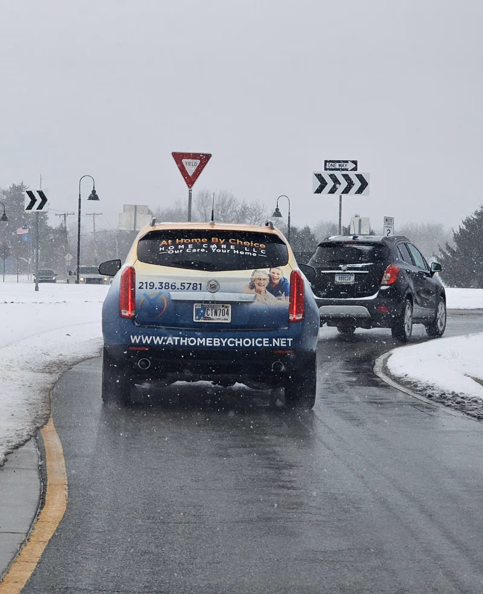 Blue SUV advertising At Home By Choice Home Care LLC on a snowy roadway.