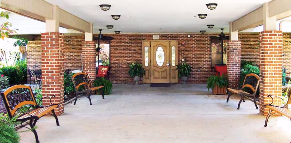 Covered brick entrance with benches, potted plants, and double wooden doors.