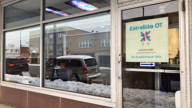 Exterior storefront of Estrellita OT with snow, windows, and a parked car.