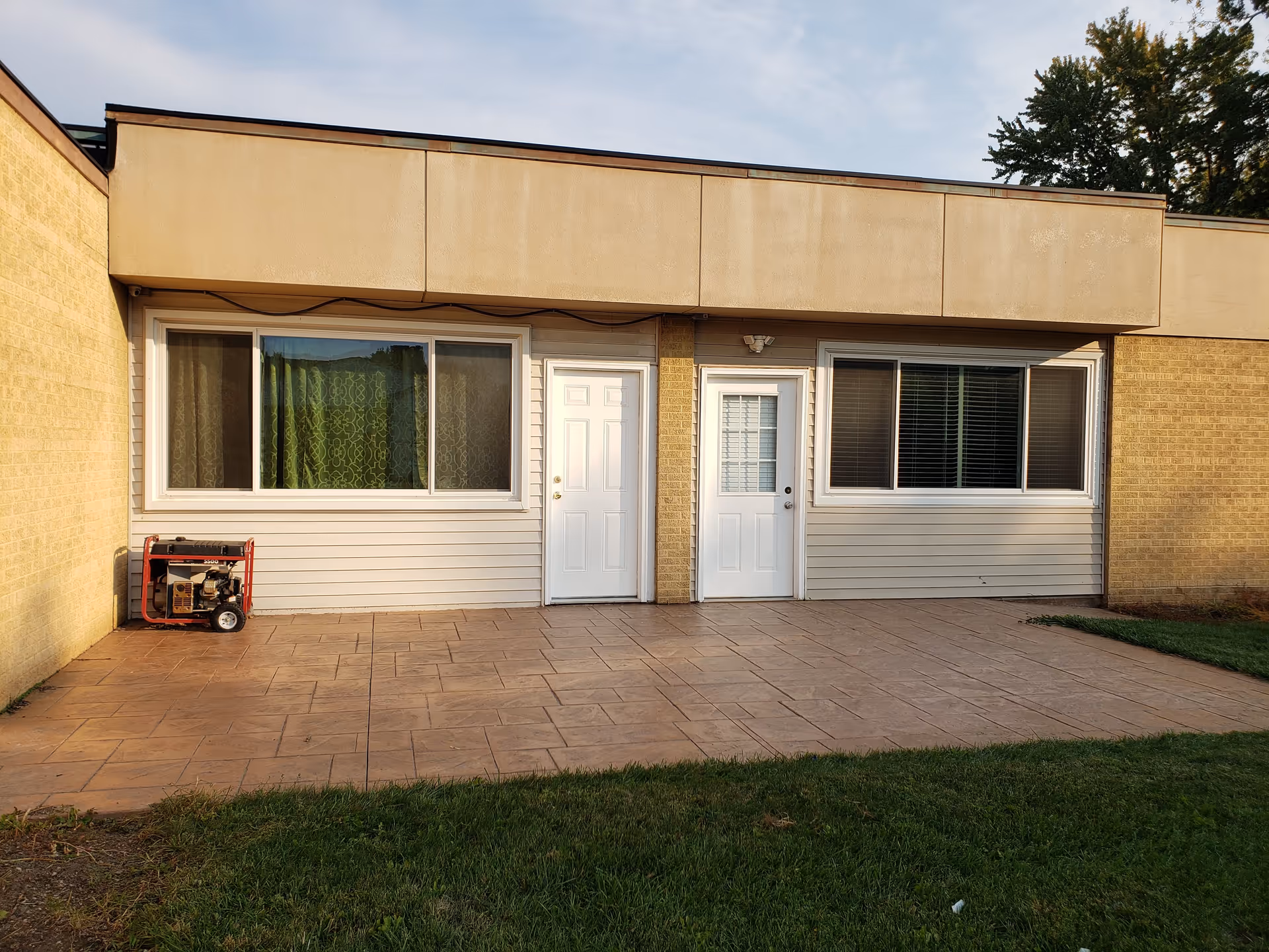 Single-story beige-brick facility exterior with two doors, large windows, and a tiled patio.