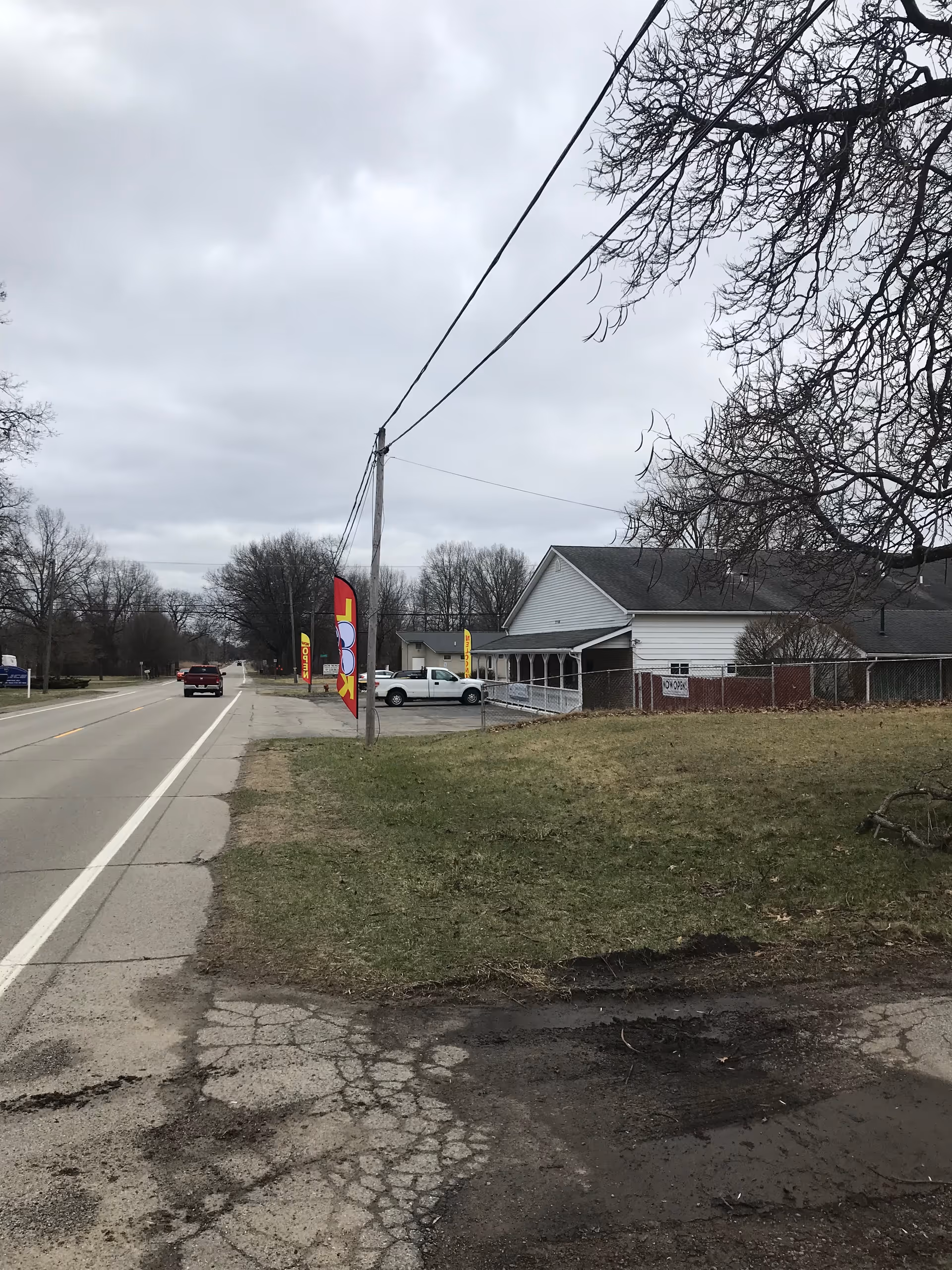 Street view showing a white facility building beside a grassy lot on a two-lane road.