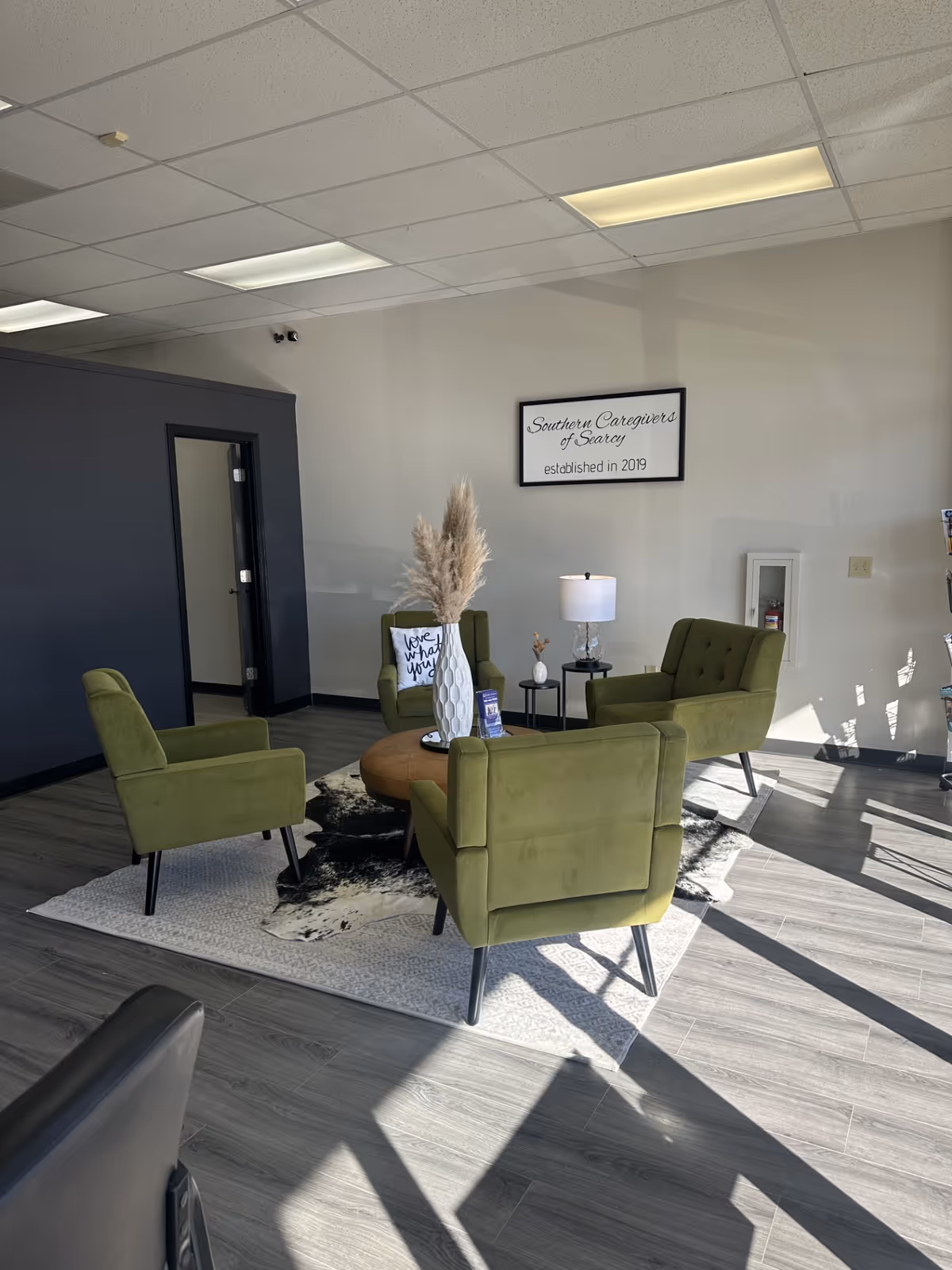 Four green chairs surround a round wooden table in a modern lobby lounge.