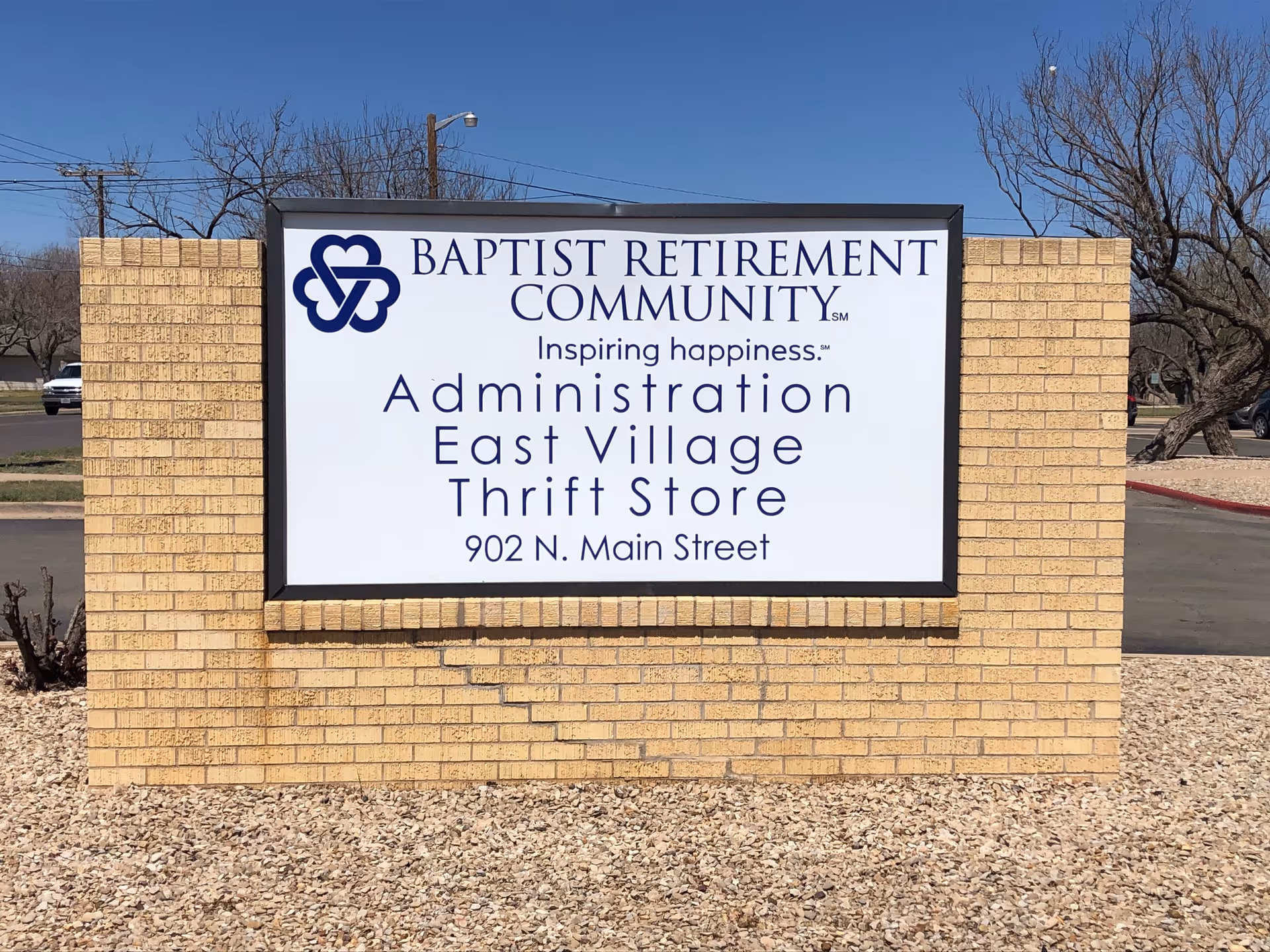 A brick monument sign reading "Baptist Retirement Community" with listings for Administration, East Village Thrift Store and the address 902 N. Main Street.