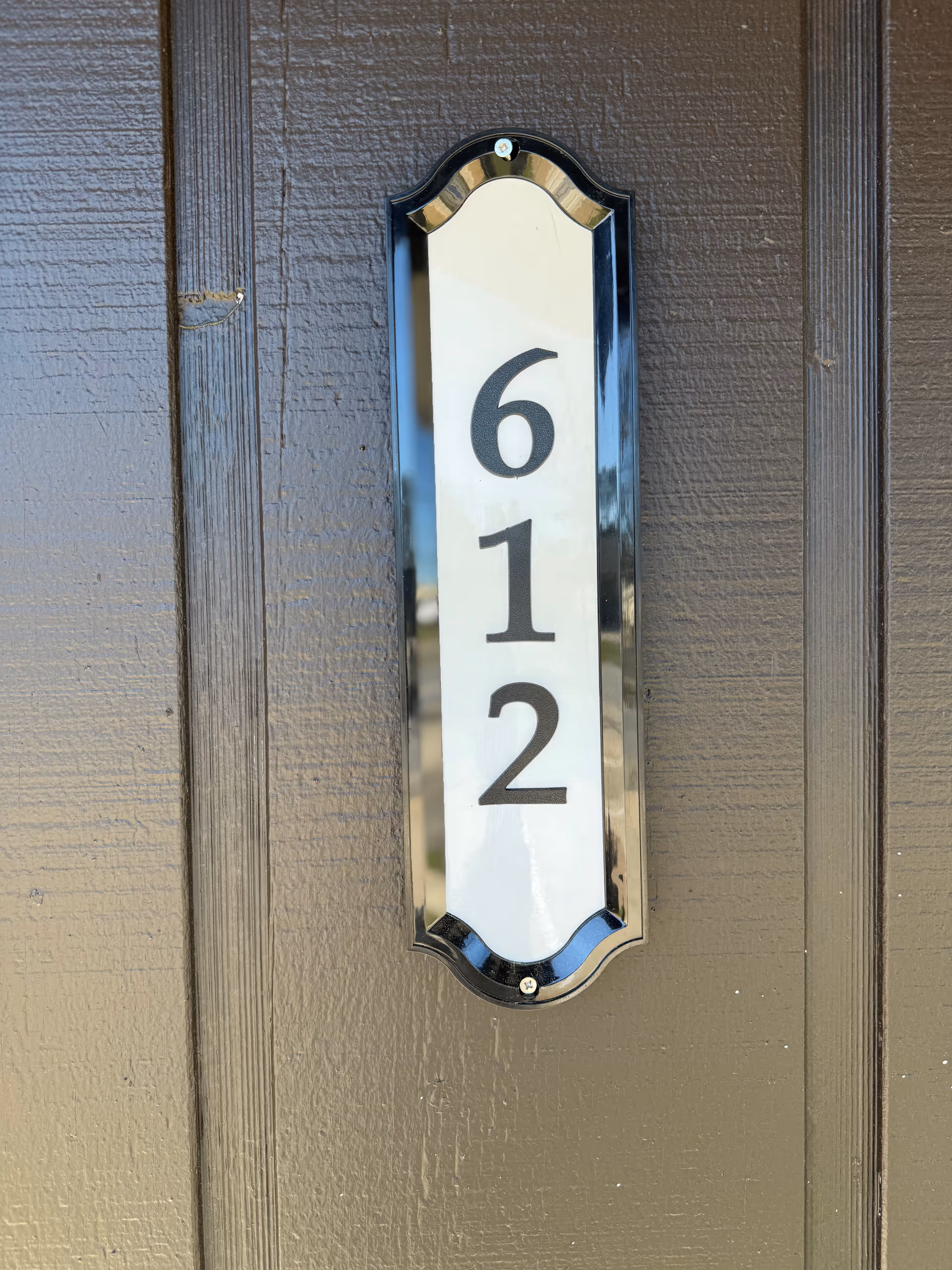 Close-up of a vertical metal door number plaque reading 612 on brown exterior wall.