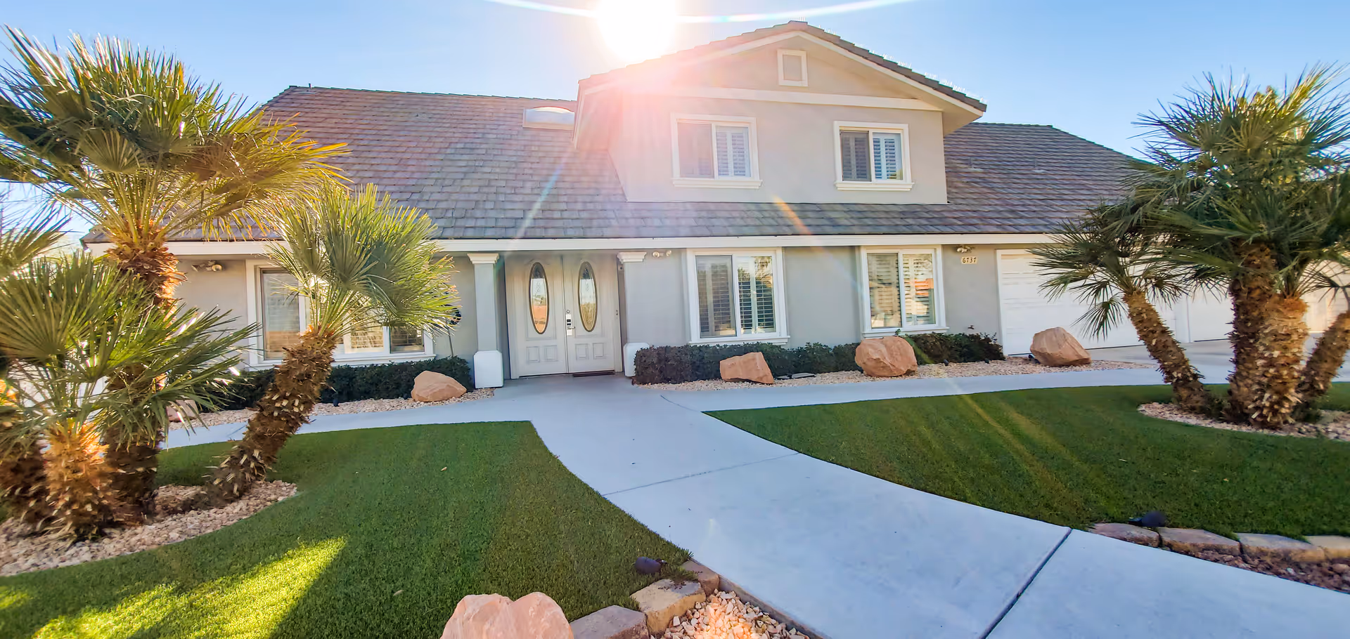 Front view of a single-story memory care home with curved walkway and palm trees.