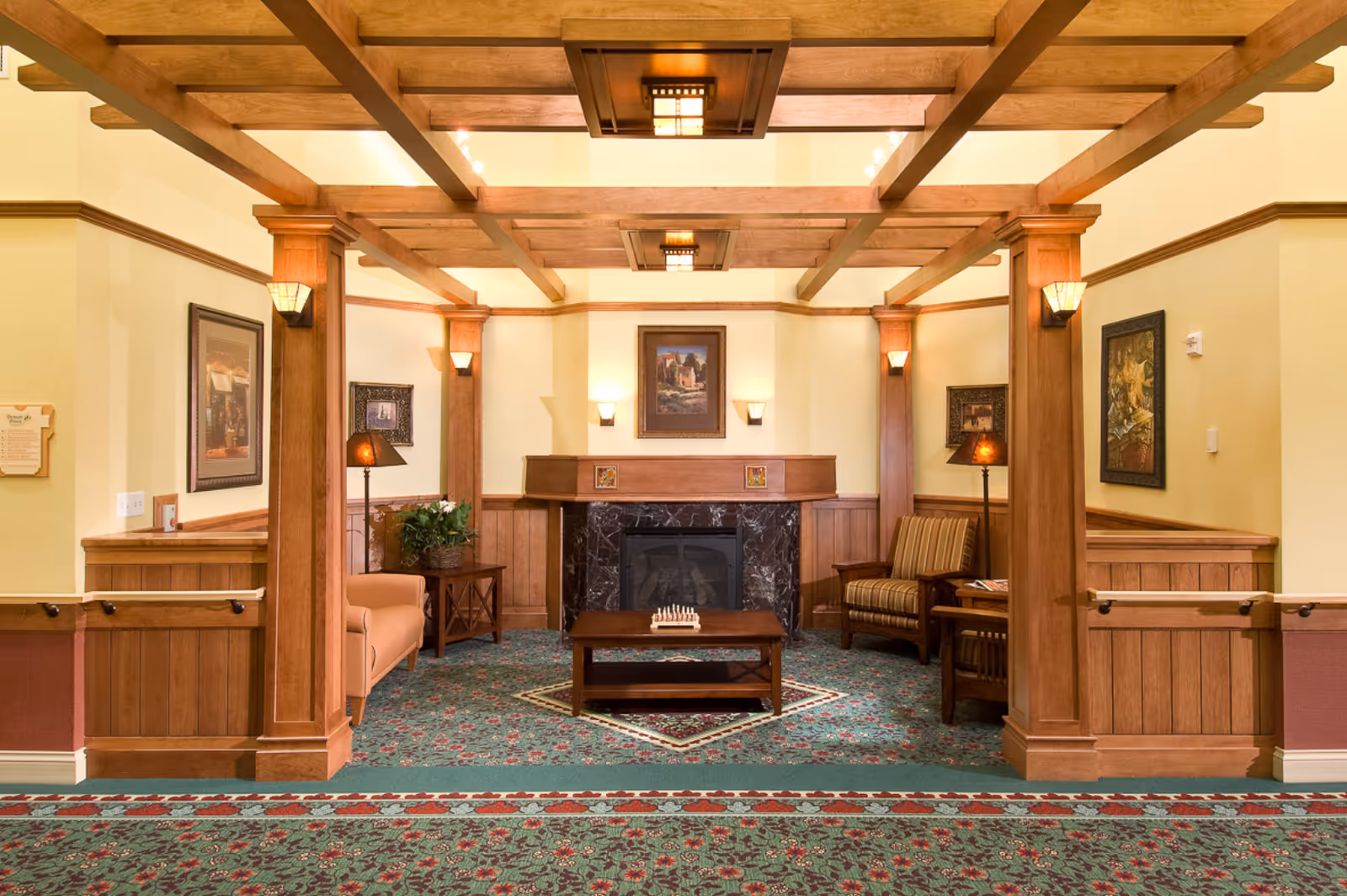 Cozy common area with exposed wooden beams, a central fireplace, seating, and patterned carpeting.