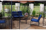 Outdoor seating area under a canopy with blue cushioned chairs, a table, and potted plants.