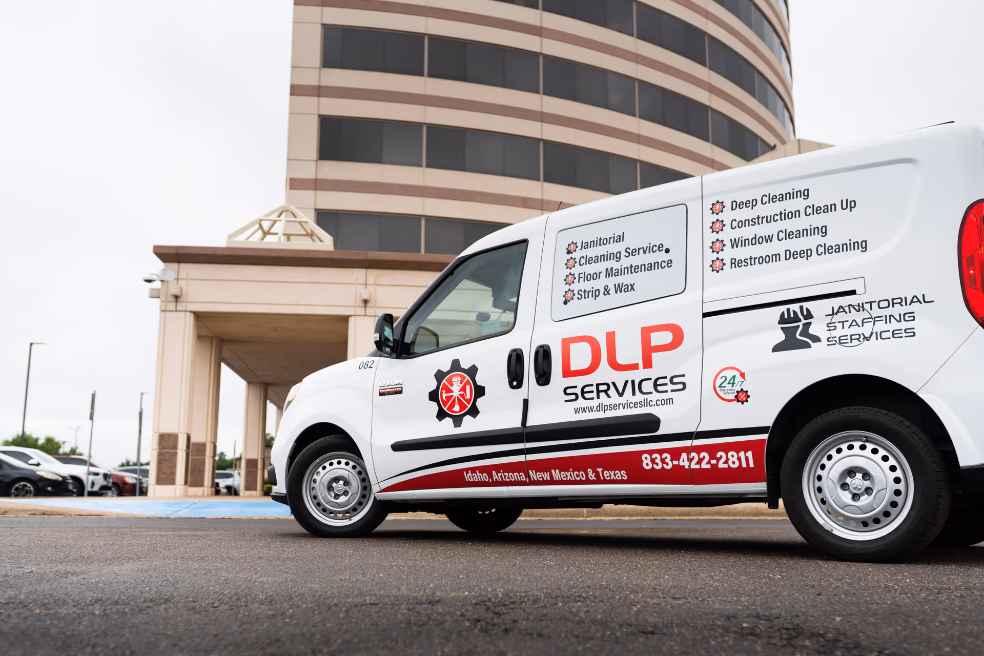 A white DLP Services van parked in front of a tall multi-story building.