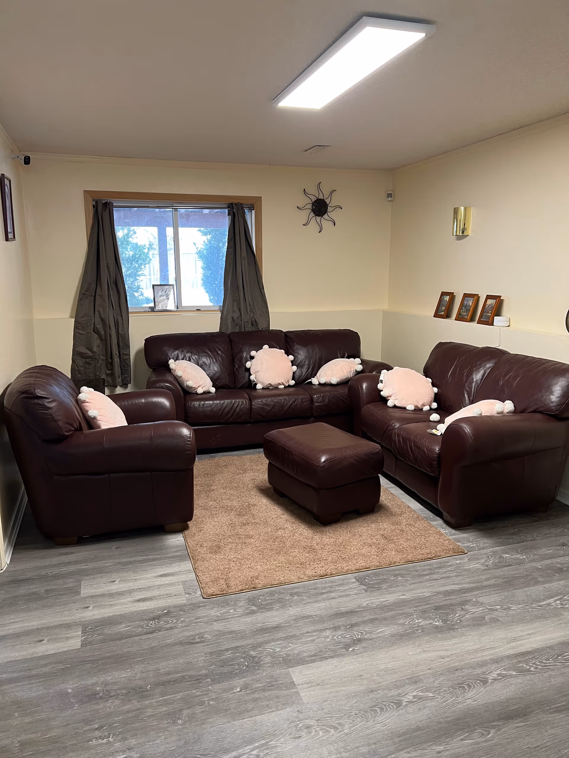 Cozy brown leather living room with sectional sofas, ottoman, window with dark curtains, and pink cushions.