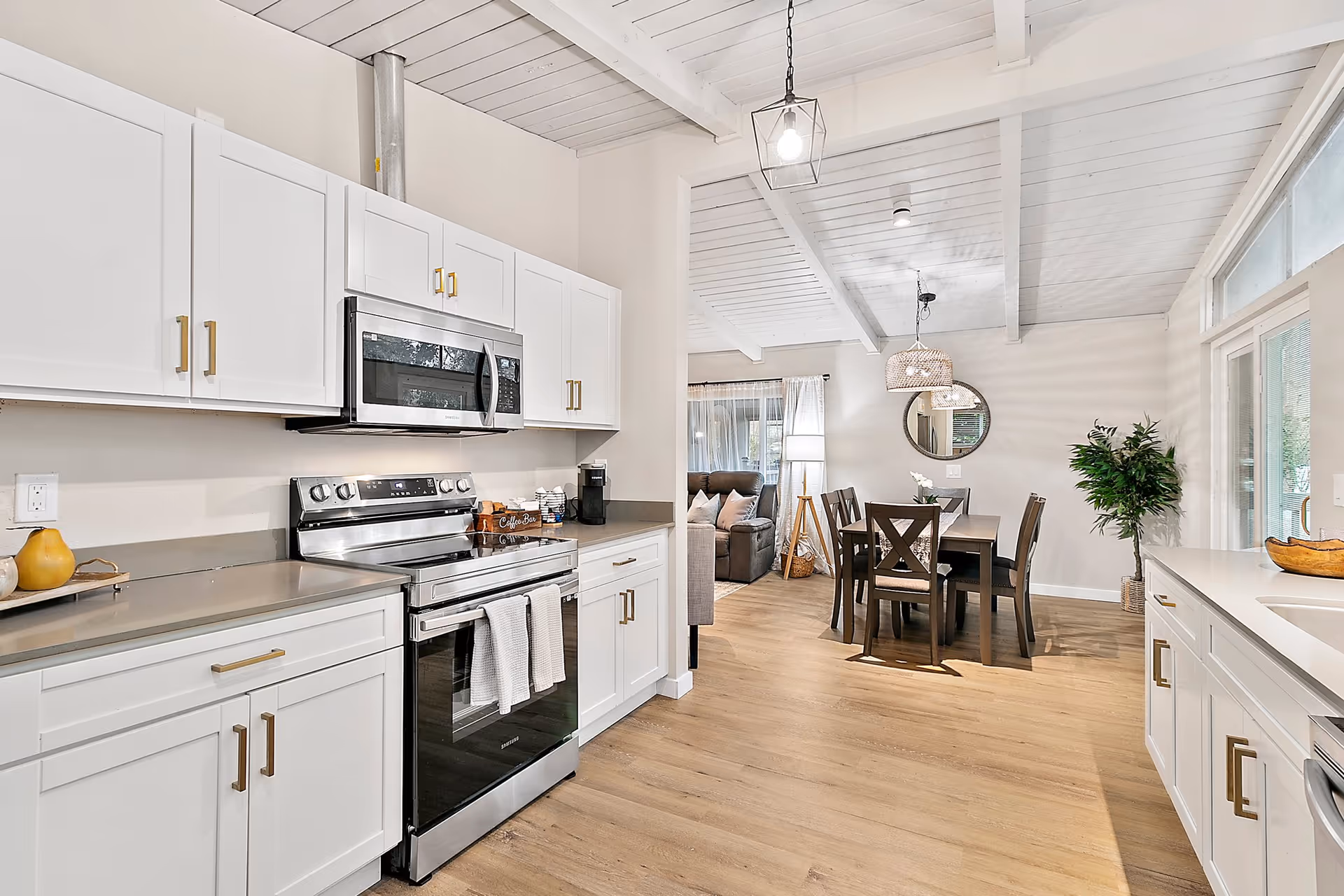 Bright white kitchen with stainless steel appliances and a dining area in the background.