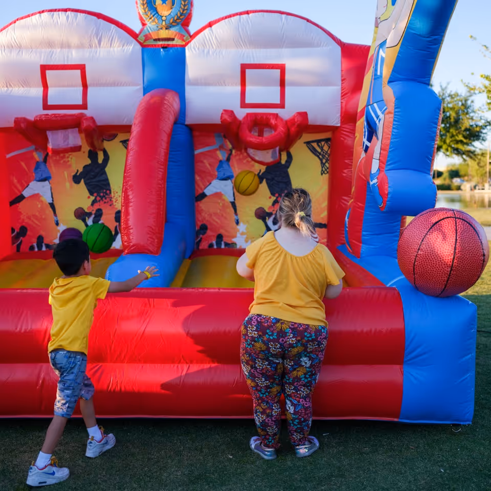 Two children play near a colorful inflatable bounce house outdoors on a grassy area.
