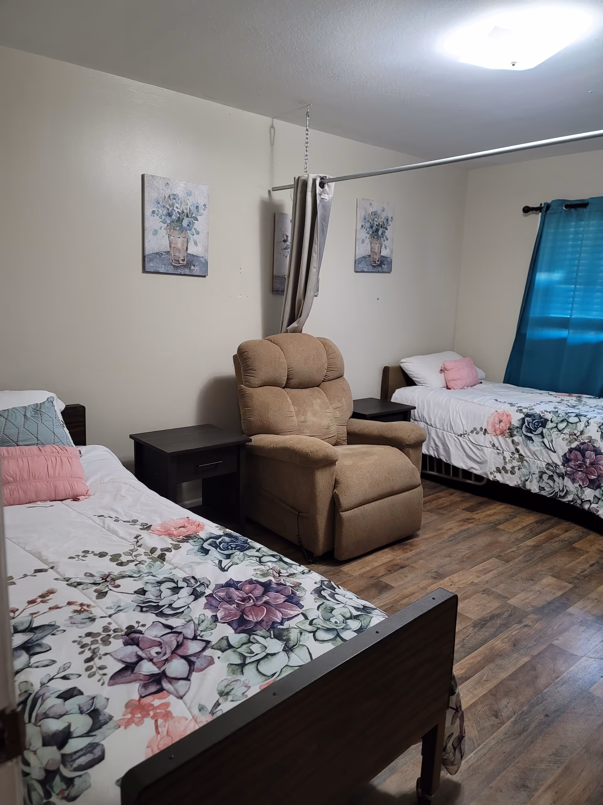 Two single beds in a shared bedroom with floral bedding and a recliner between them.