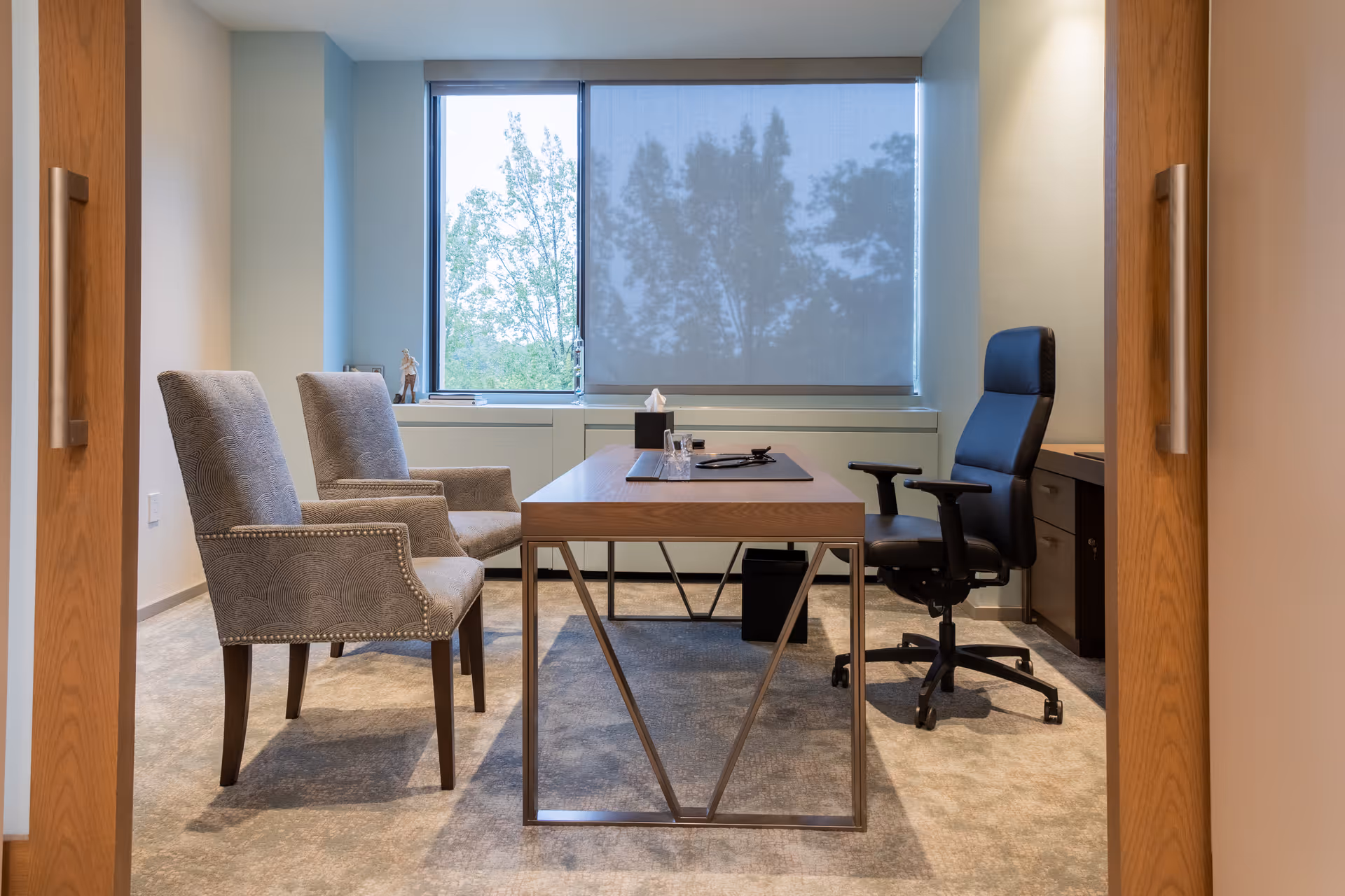 A modern private office with a desk, two guest chairs, and a large window.