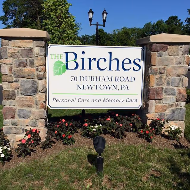 Outdoor sign for The Birches at Newtown with stone pillars and flowers.
