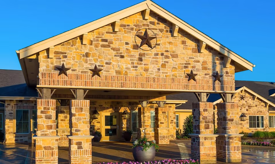 Stone-faced senior living facility entrance with brick columns and star accents under blue sky
