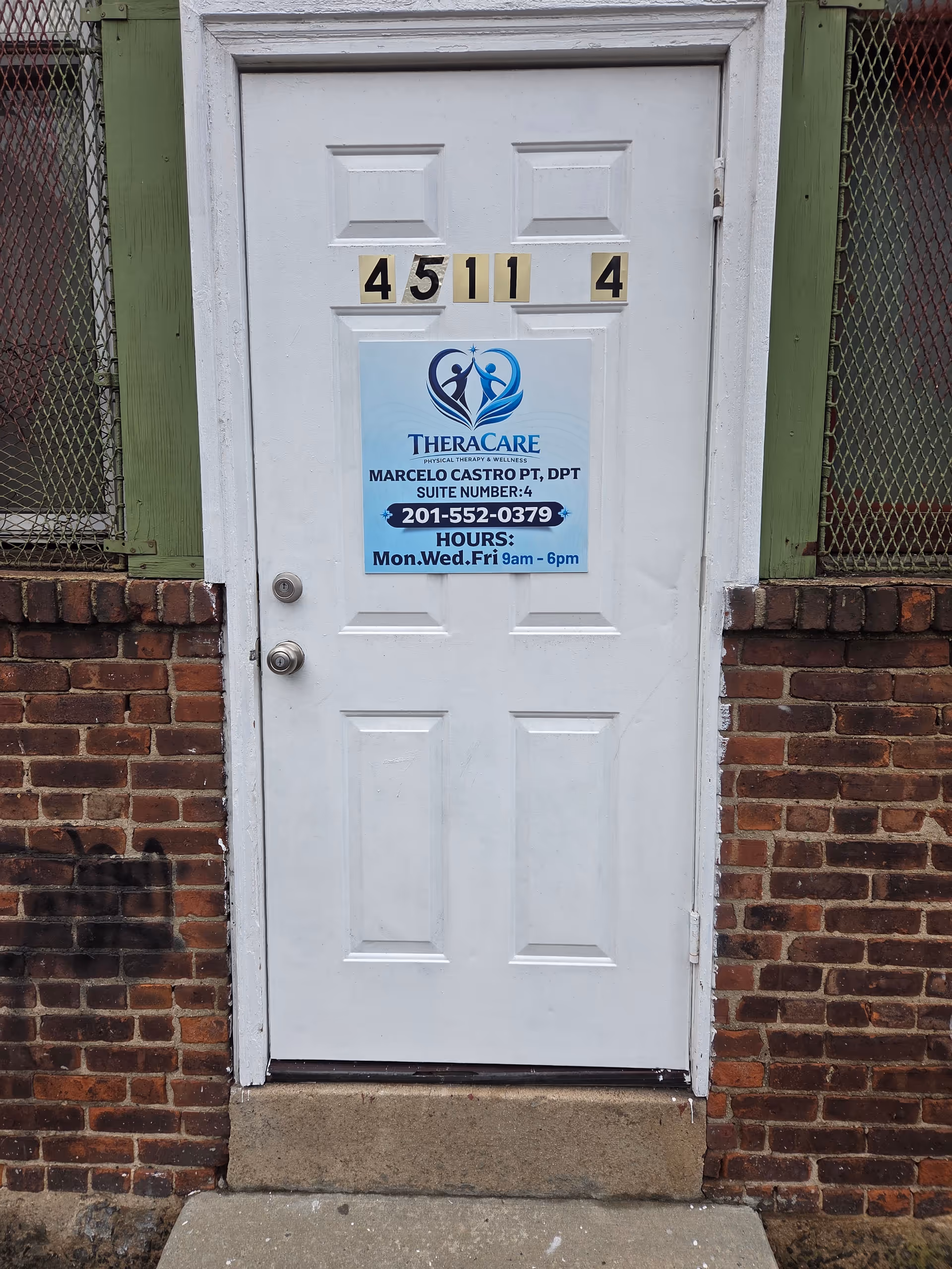 White entrance door with a TheraCare poster on brick exterior wall.